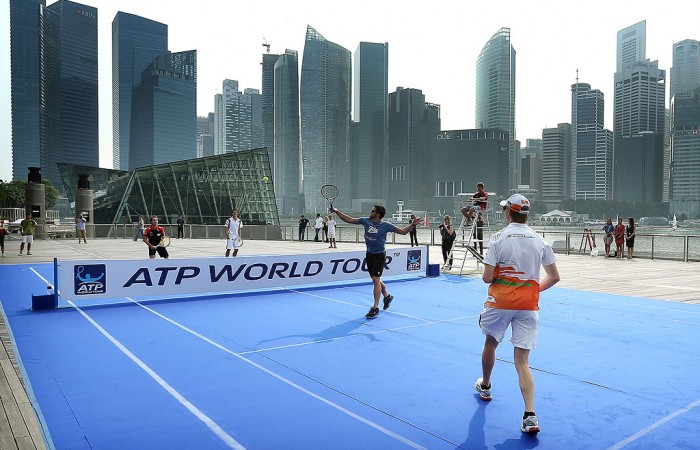 Janko Tipsarevic of Serbia returns a shot as doubles partner Nico Hulkenberg of the Force India Formula 1 racing team watches on in a match on a temporary court placed on Singapore's Marina Parade promenade during the ATP World Tour's promotion of its Asian swing; Getty Images for ATP